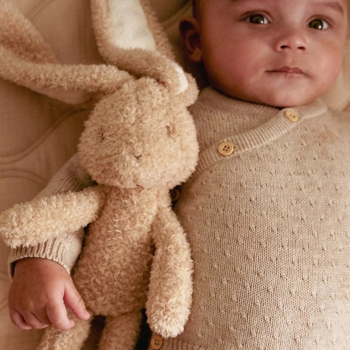 Baby holding a soft toy, both in beige clothing