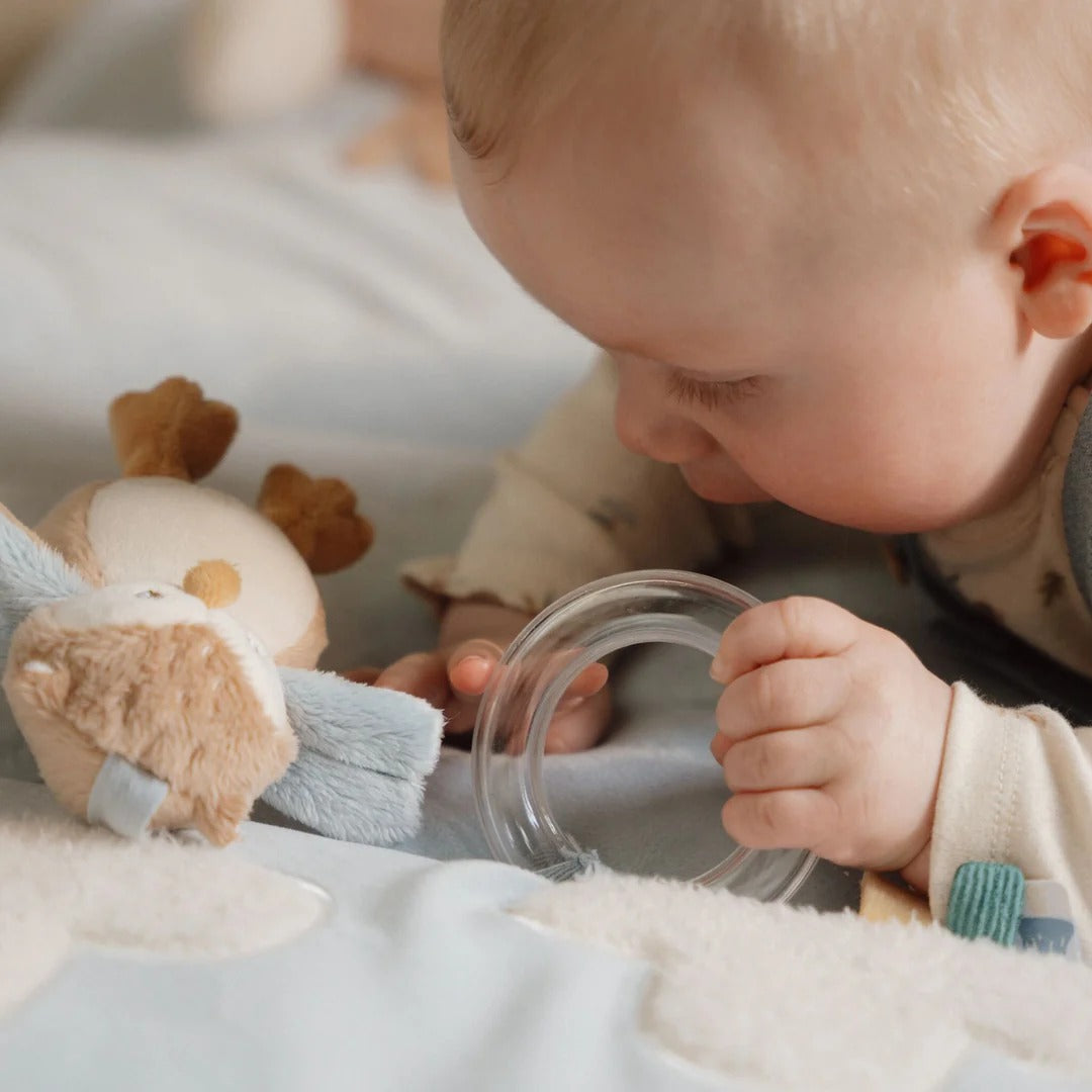 Baby playing with a clear container and plush toy on a soft surface