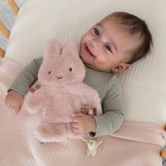 Baby holding a pink plush toy on a soft surface