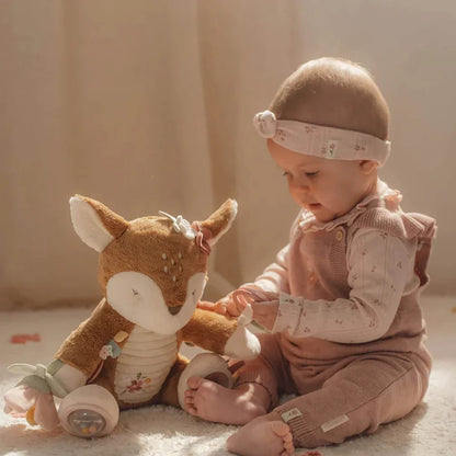 Baby in pink outfit playing with a plush deer toy on a soft surface.