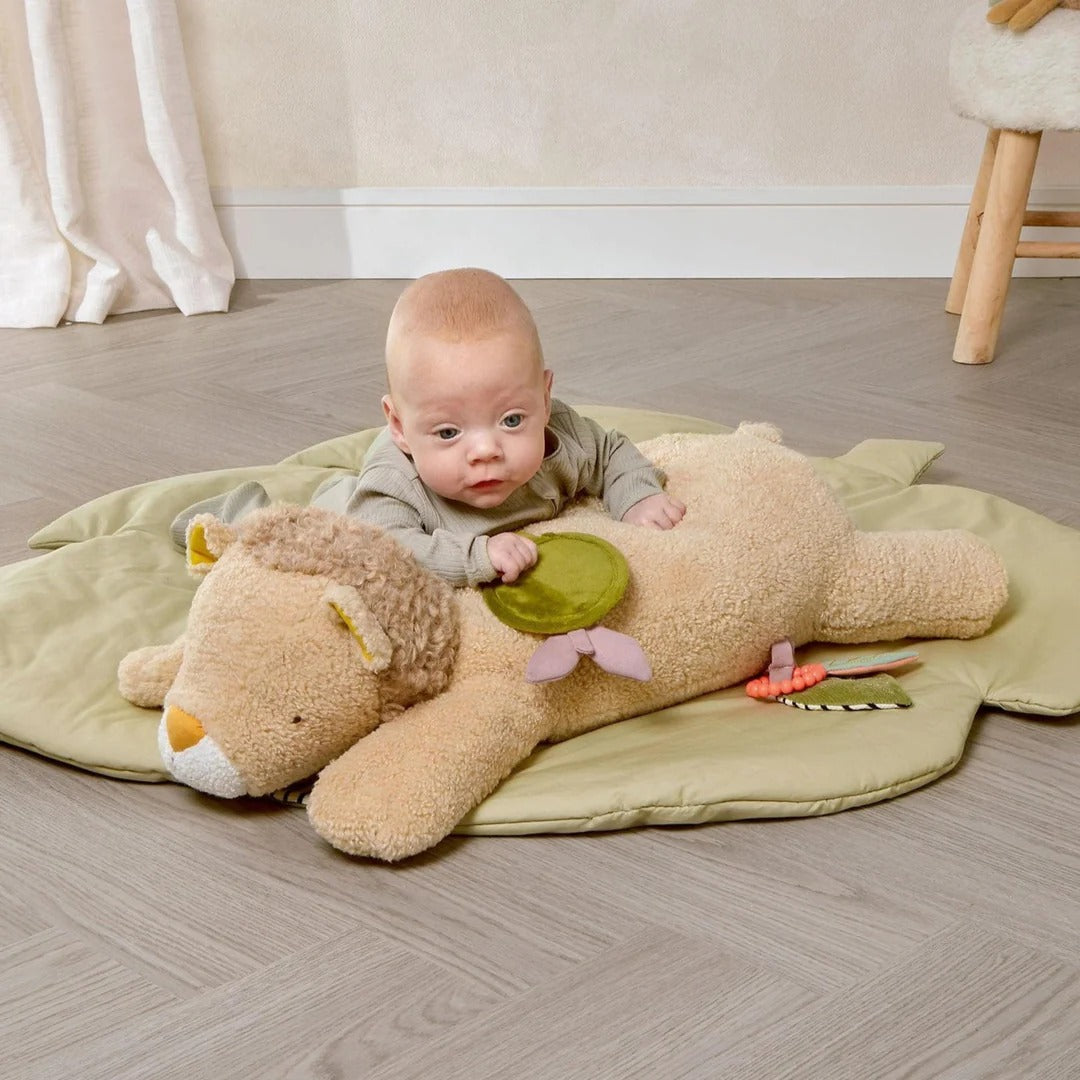Baby lying on a large teddy bear toy on a wooden floor.