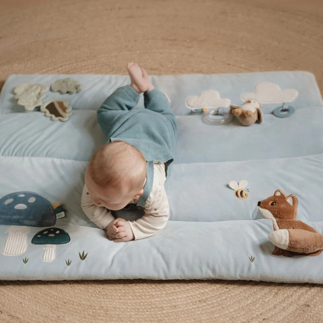 Baby lying on a soft play mat with toys on a beige carpet