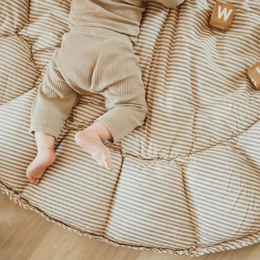 Baby lying on a striped cushion with wooden blocks nearby