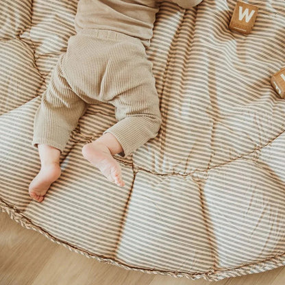 Baby lying on a striped cushion with wooden blocks nearby