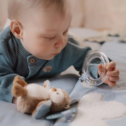 Baby playing with a teething ring and soft toy on a blanket