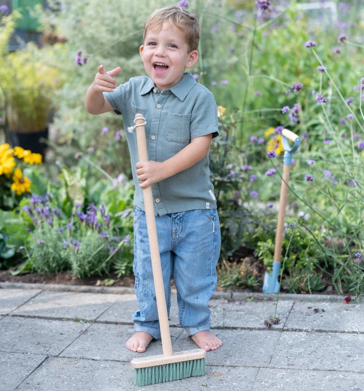 Child holding a broom in a garden setting