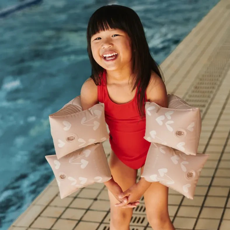 Child in a red swimsuit holding pink arm floats by a pool