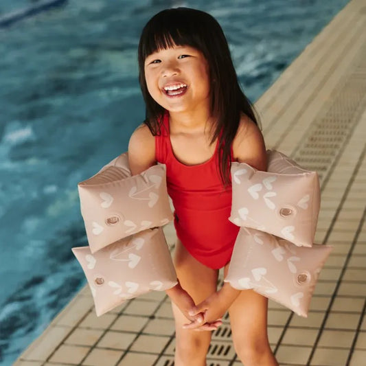 Child in a red swimsuit holding pink arm floats by a pool