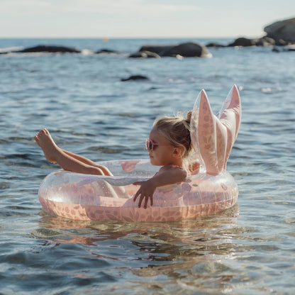 Child on a transparent inflatable pool float with pink bunny ears in the water.