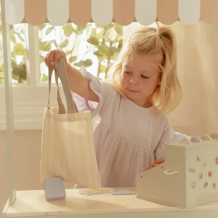 Child playing with a toy cash register and bag in a bright room.