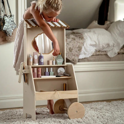 Child playing with a wooden dollhouse vanity set in a bedroom.