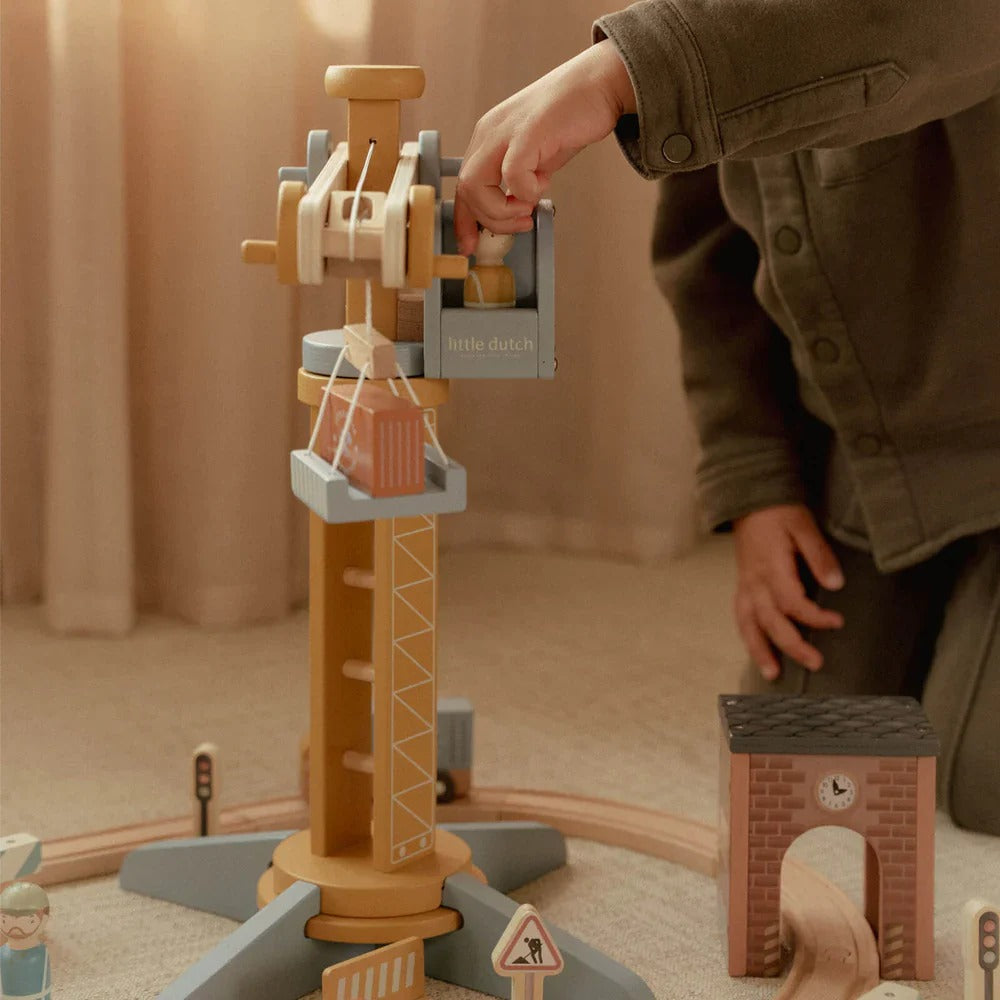 Child playing with a wooden toy crane set on a carpeted floor.