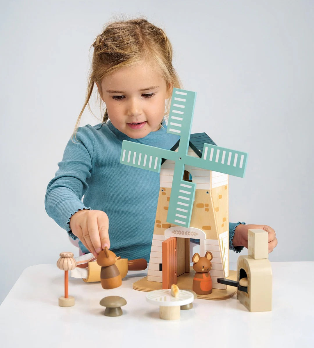 Child playing with a wooden toy windmill set on a white surface.
