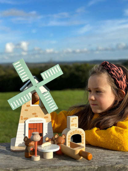 Child playing with a wooden toy windmill set outdoors on a sunny day.