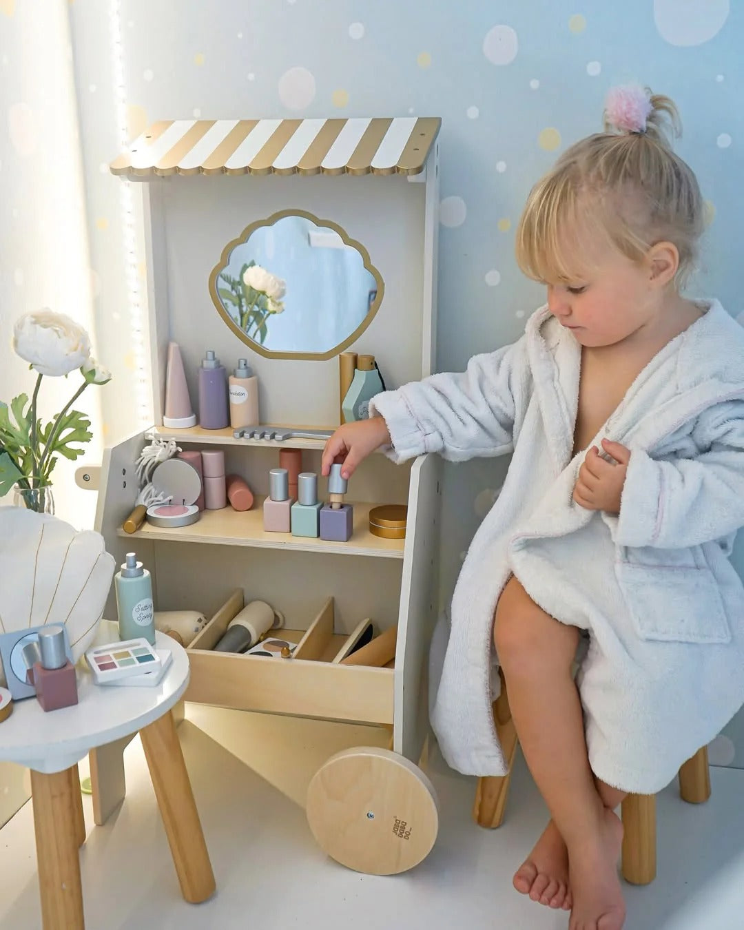 Child playing with toys in a playroom setup with a small wooden house and mirror.