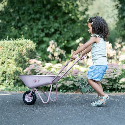 Child pushing a pink wheelbarrow in a garden setting