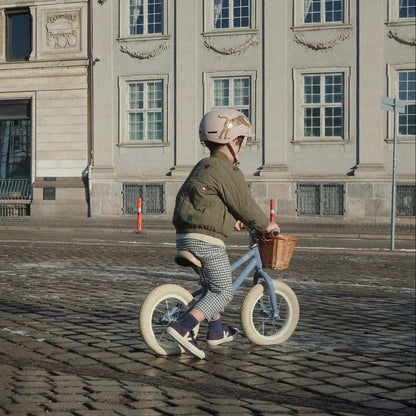 Child riding a balance bike on a cobblestone street with a large building in the background