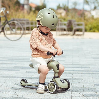 Child riding a green tricycle with a helmet on a paved path.