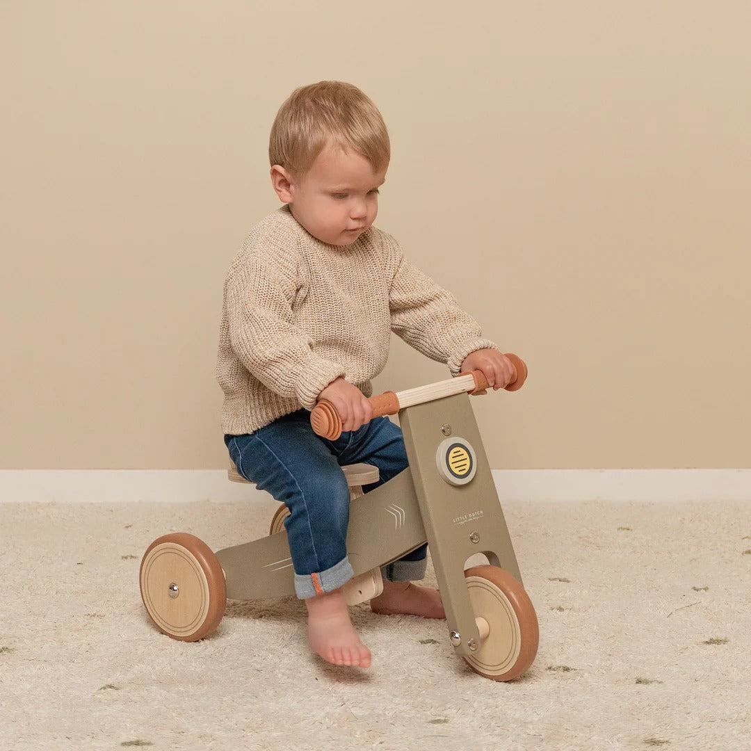 Child riding a wooden balance bike on a neutral background