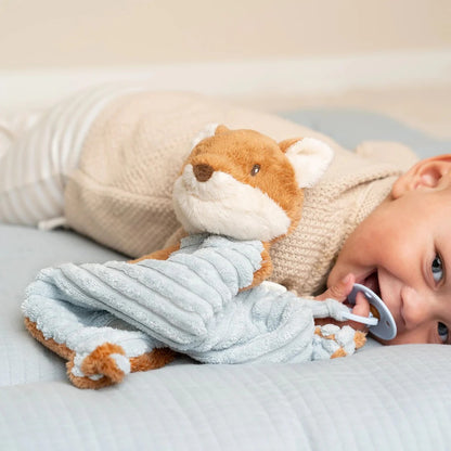 Child with a plush fox toy and pacifier on a bed