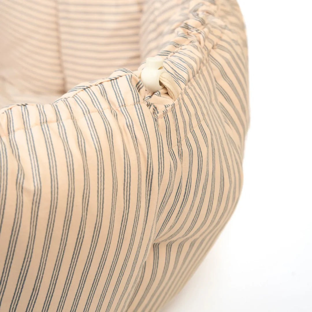Close-up of a beige pet bed with striped pattern and button detail on a white background