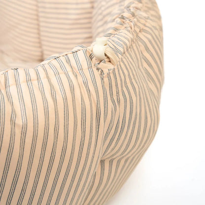 Close-up of a beige pet bed with striped pattern and button detail on a white background