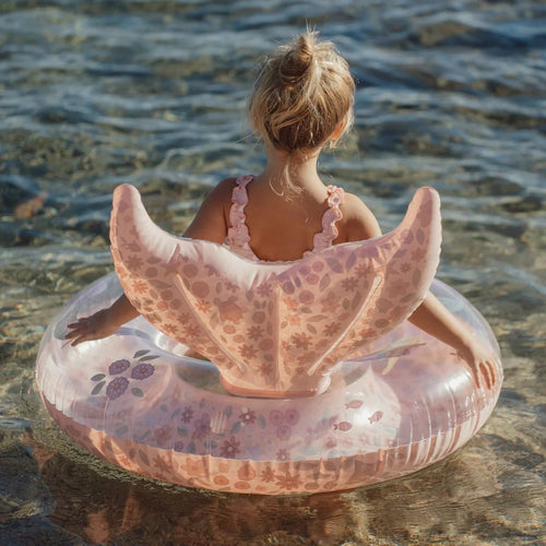 Person sitting on a floral inflatable ring in shallow water.