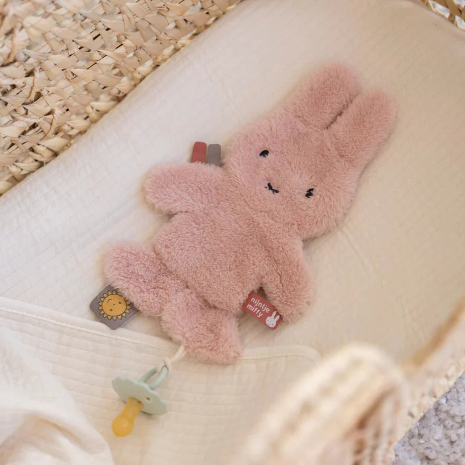Pink bunny plush toy with a pacifier on a textured surface