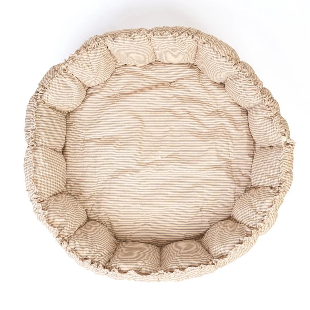 Round beige pet bed with textured surface on a white background