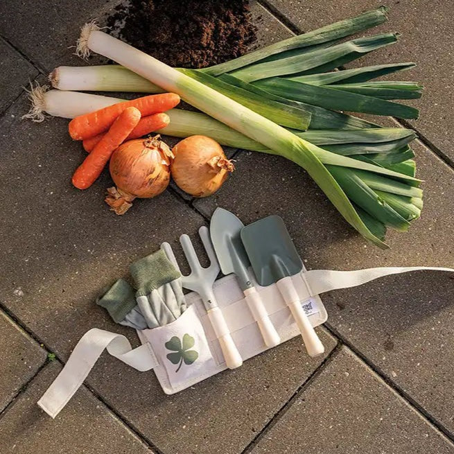 Set of gardening tools with a pouch on a stone surface with vegetables.