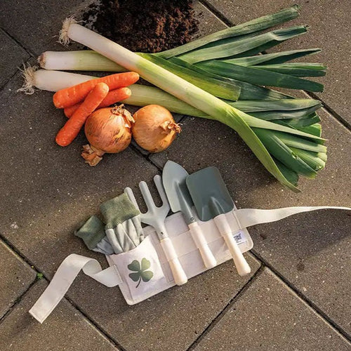 Set of gardening tools with a pouch on a stone surface with vegetables.