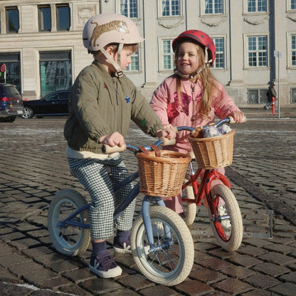 Two children on balance bikes with baskets in an urban setting