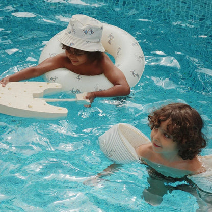 Two children playing in a pool with inflatable rings and a paddle.