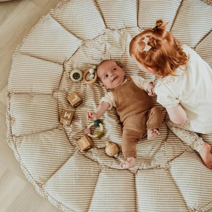 Two children playing on a large textured cushion with wooden toys.