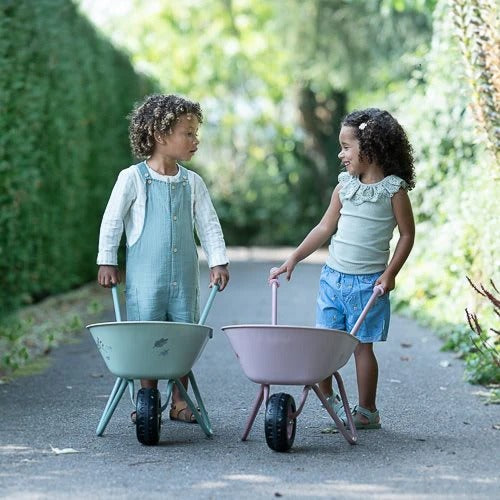 Two children playing with wheelbarrows in a garden.