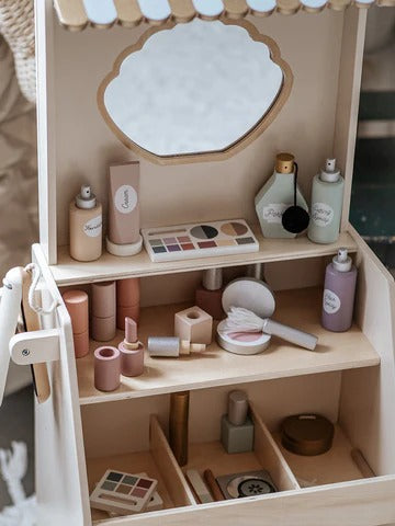 Wooden makeup station with various cosmetic items and a mirror on a neutral background